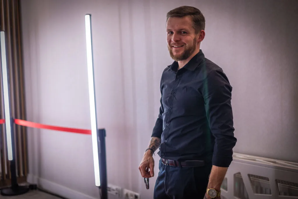 Uśmiechnięty gość w granatowej koszuli obok podświetlanych lamp LED